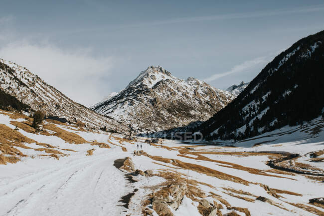 Silhuetas de pessoas andando em terras selvagens entre colinas de pedra na neve em dia ensolarado — Fotografia de Stock