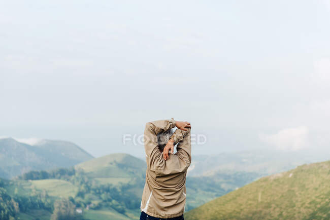 Вид ззаду на невизначену старшу жінку-мандрівника, що піднімає і розтягує руки вранці на горбистій місцевості — стокове фото