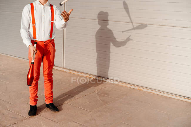 Обрезанный неузнаваемый опытный молодой цирковой артист, жонглирующий клубом на современном здании — стоковое фото