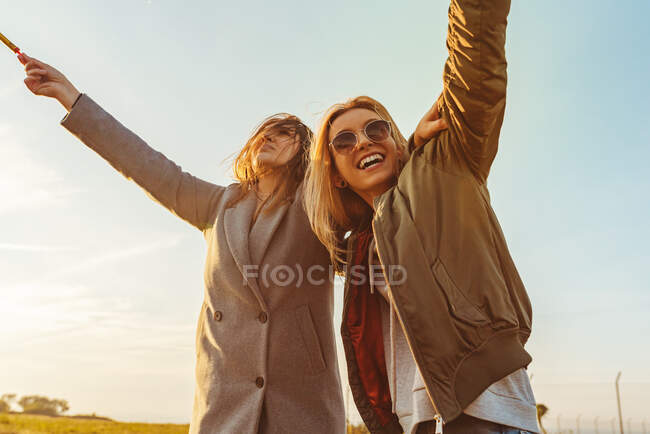 Cheerful females with sparkling candles embracing on meadow in mountains having fun at sunset — Stock Photo