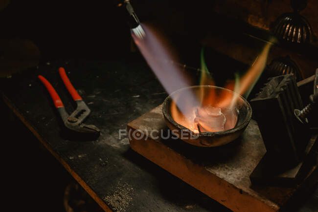 Unrecognizable goldsmith melting metal for jewellery with blowtorch while standing near workbench in workshop — Stock Photo