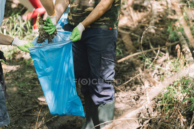 Grupo de niños sociales activos con el hombre voluntario recogiendo basura en la bolsa de basura durante la campaña ambiental en la naturaleza de verano - foto de stock