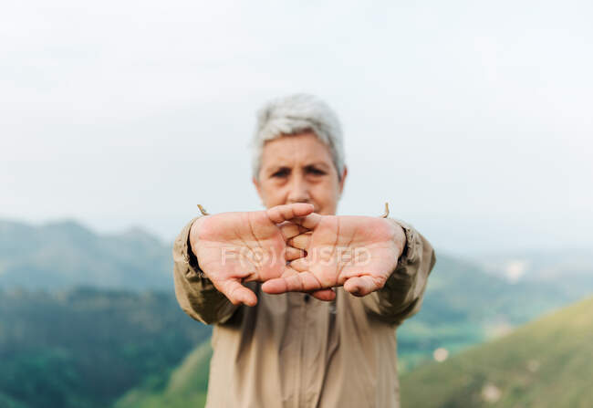 Focus doux de voyageuse âgée étirant les bras et se réchauffant pendant le voyage en terrain vallonné — Photo de stock