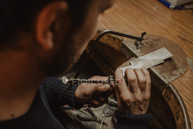 Unrecognizable goldsmith cutting metal with saw while making jewellery in workshop — Stock Photo