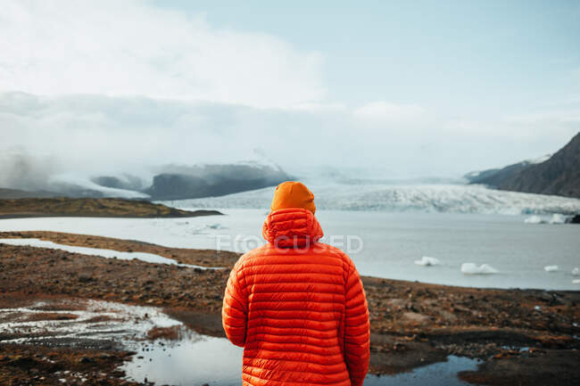 Back view of young tourist on peak of mountain in snow looking at water in valley — Stock Photo