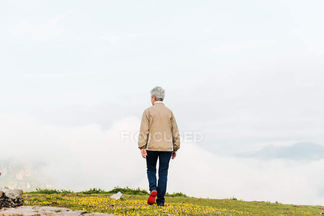 Вид на неузнаваемую старшую женщину-путешественницу, идущую утром по холмистой местности — стоковое фото