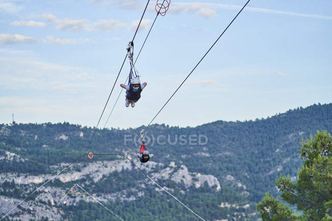 Pessoas corajosas anônimas em equipamentos de segurança montando tirolesa sobre montanhas no verão — Fotografia de Stock