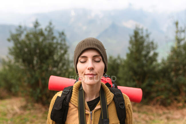 Mochila fêmea despreocupada em pé em terras altas com olhos fechados e desfrutando da natureza durante a viagem no verão — Fotografia de Stock