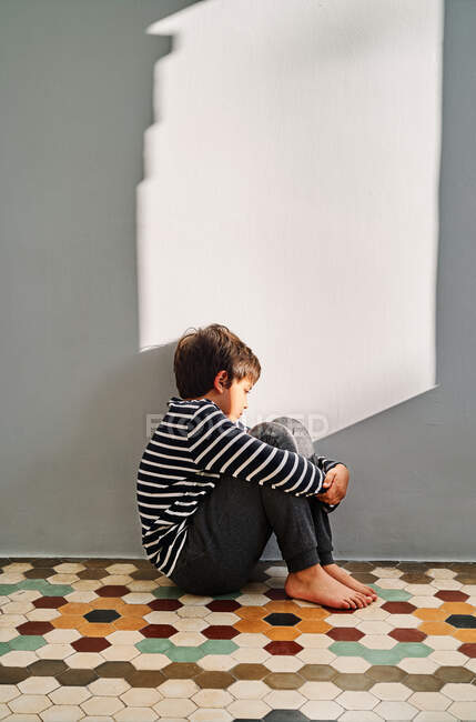 Sid vista del bambino infelice seduto sul pavimento e che copre la testa con le mani mentre soffre di violenza domestica in casa — Foto stock