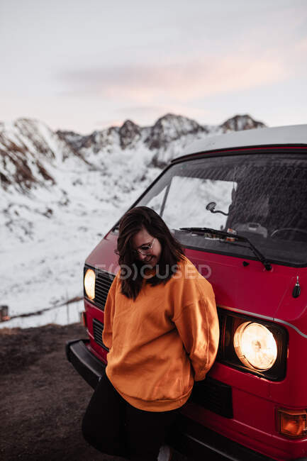 Jeune touriste heureux dans des lunettes debout près de l'automobile vintage entre le sol désert dans la neige près des montagnes — Photo de stock