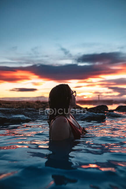 Side view of young woman in swimsuit posing in blue water between rocks — Stock Photo