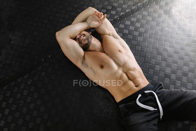 From above tired sportsman lying down on gym floor resting during training at the gym — Stock Photo