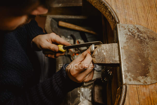 Gioielliere maschio anonimo che utilizza il file per modellare l'anello metallico sul banco da lavoro in officina — Foto stock