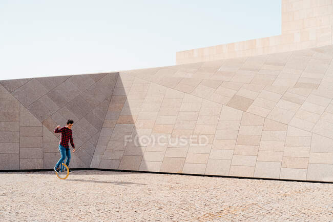 Side view of male riding unicycle against contemporary stone construction of unusual geometric shape — Stock Photo