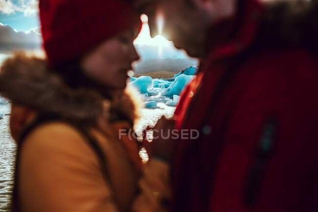 Вид збоку молодого чоловіка і жінки в зимовому одязі, що стоїть біля води з льодом — стокове фото