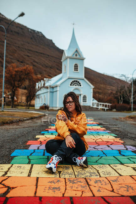 Jovem turista sentado na rua entre edifícios de aldeia perto da catedral e montanha — Fotografia de Stock