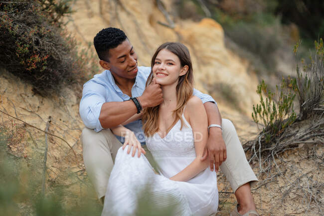 Conteúdo casal multirracial de recém-casados sentados na floresta e abraçando no dia do casamento — Fotografia de Stock