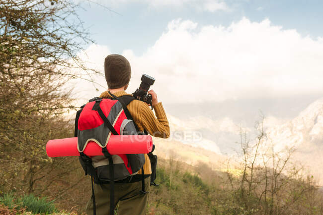 Vista posterior de una mochilera anónima tomando fotos del paisaje montañoso durante el viaje - foto de stock