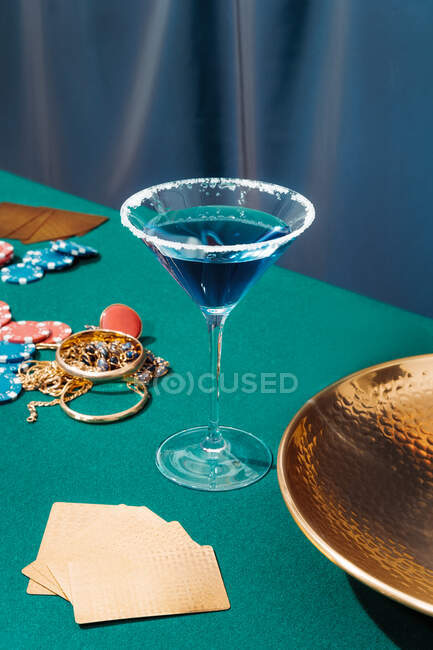 Green poker table with cards and chips placed near jewelry and glasses with alcohol cocktails — Stock Photo