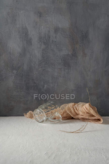 Copo de vidro e pano colocado com galho de árvore no fundo bege e cinza — Fotografia de Stock