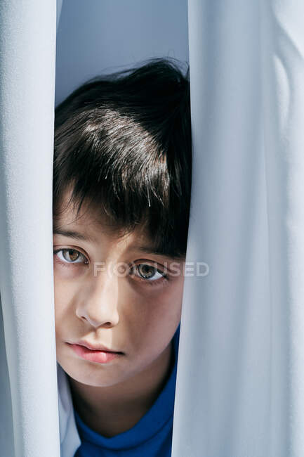 Ragazzino infelice sbirciare fuori da dietro le tende mentre soffre di violenza domestica e si nasconde dai genitori — Foto stock