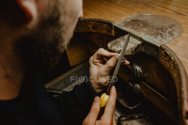 Bijoutier masculin anonyme utilisant un fichier pour façonner une bague en métal sur un établi en atelier — Photo de stock