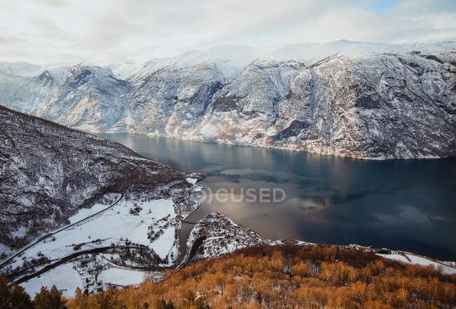 Dall'alto cima della collina con pittoresca vista sulle montagne sulla neve sulla riva vicino alla superficie dell'acqua — Foto stock