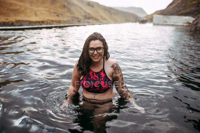 Jeune hipster tatoué joyeux en maillot de bain dans l'eau entre les montagnes — Photo de stock