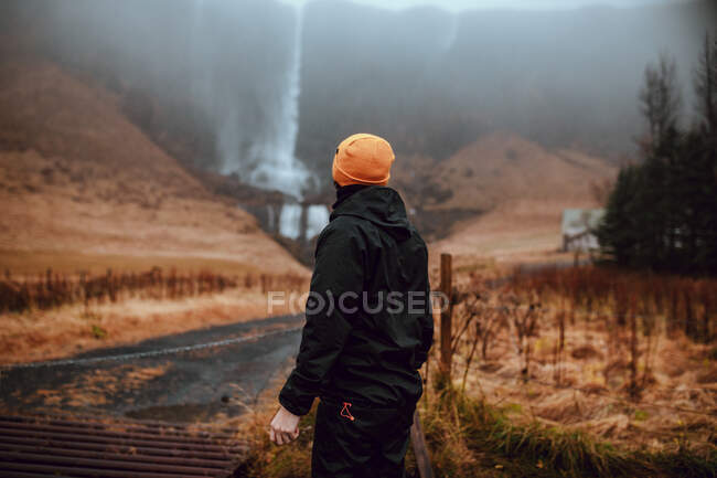 Visão traseira do turista jovem em desgaste de inverno olhando para cascata e rio de montanha entre colina de pedra — Fotografia de Stock