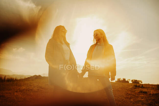 Novias tomadas de las manos suavemente de pie en la lente destello de luz puesta del sol en la naturaleza - foto de stock
