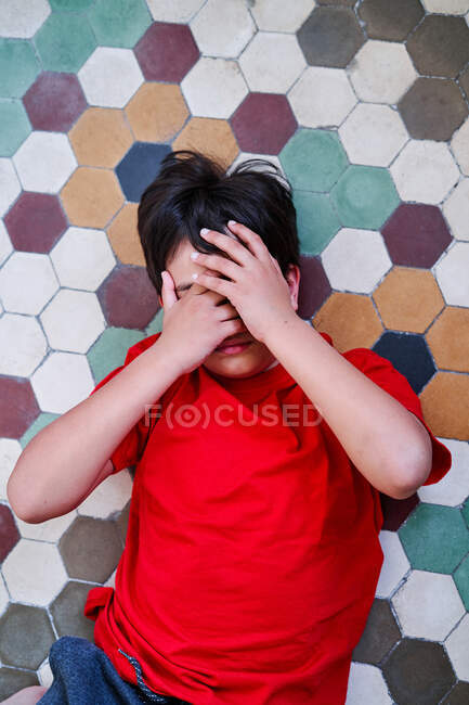 Von oben ein unglücklicher einsamer, auf dem Boden liegender Junge, der sein Gesicht als Opfer häuslicher Gewalt und Missbrauch versteckt — Stockfoto