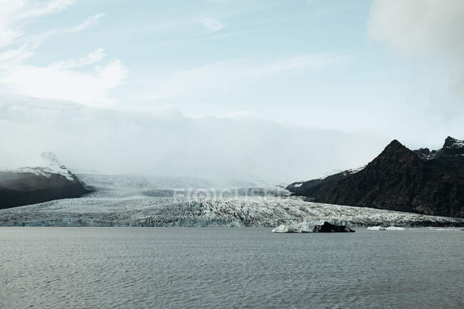 Мальовничий вид на поверхню води біля дивовижного величезного льодовика між скелястими пагорбами і блакитним небом — стокове фото