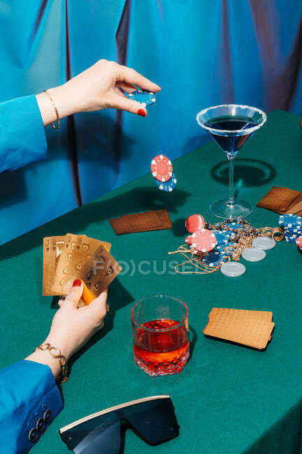 Cosecha hembra irreconocible con cartas y fichas jugando al póquer mientras estás sentado en la mesa verde - foto de stock