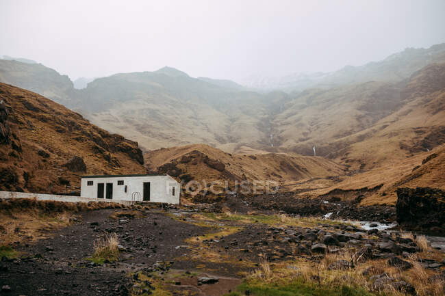Cabanas envelhecidas perto de paredes rochosas entre terras selvagens perto de rio estreito — Fotografia de Stock