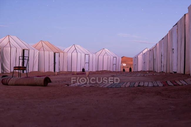 Beaucoup de chaises de tentes blanches et des tapis sur le sable avec ciel clair en soirée bleue sur le fond au Maroc — Photo de stock
