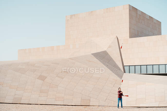 Full length of unrecognizable male performing trick with juggling clubs while standing against contemporary stone building with unusual geometric architecture — Stock Photo