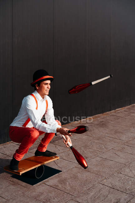 Full body of agile professional young male circus performer juggling clubs and balancing on board — Stock Photo