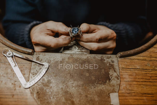 Anonymous jeweler holding unfinished ring in dirty hands and checking quality in workshop — Stock Photo