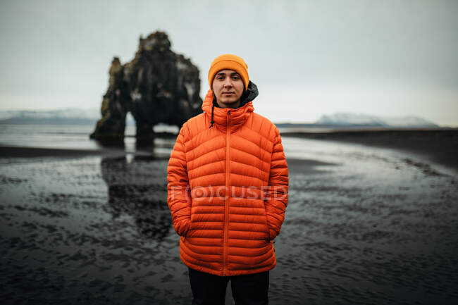 Jovem turista perto de terra na água e grande penhasco de pedra no fundo borrado — Fotografia de Stock