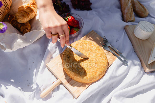 De haut de la récolte anonyme femelle coupe focaccia cuit au four tout en ayant pique-nique avec des baies croissant et fromage — Photo de stock