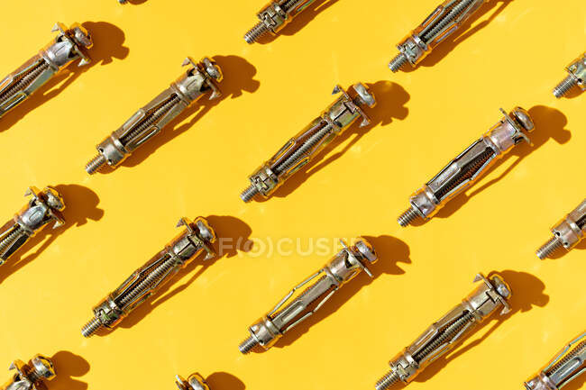 Overhead-Ansicht von strukturierten Hintergrund, der ähnliche metallische Anker mit Schrauben auf gelbem Hintergrund mit Schattierungen darstellt — Stockfoto