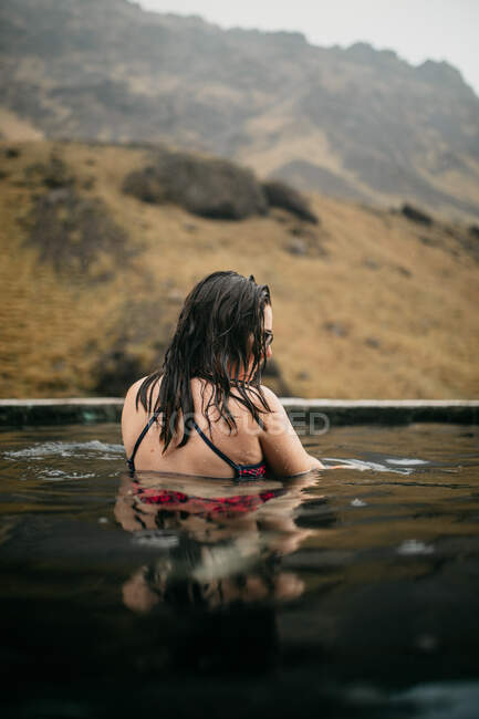 Вид сзади татуированный хипстер в купальнике в воде между горами — стоковое фото