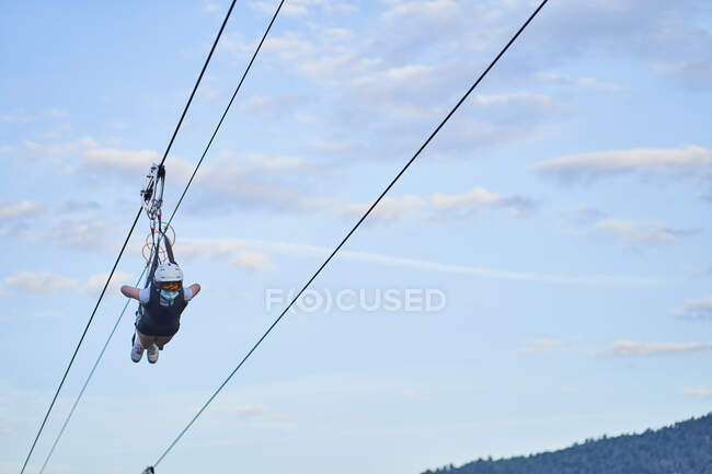 Anonymous brave man in safety equipment riding zip line over mountains in summer — Stock Photo