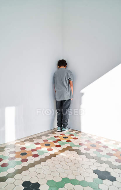 Зворотній погляд на невпізнаваного засмученого хлопчика, який був покараний і стоїть в кутку, страждаючи від домашнього насильства — стокове фото