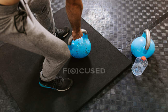 Засеянный неузнаваемый атлетичный мужчина делает упражнения с тяжелыми гирями во время активных тренировок в спортивном центре — стоковое фото