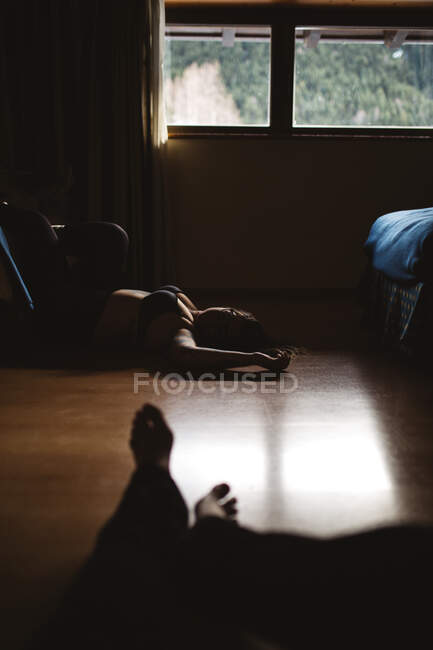Junge tätowierte nachdenkliche Frau in Dessous ruht im Dunkeln auf dem Boden — Stockfoto