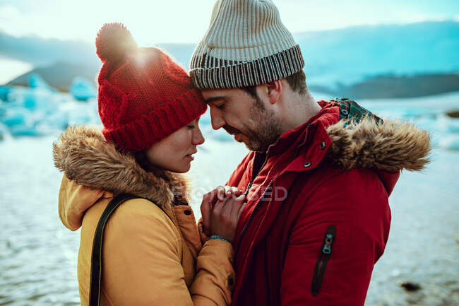 Вид збоку молодого чоловіка і жінки в зимовому одязі, що стоїть на березі біля води з льодом — стокове фото