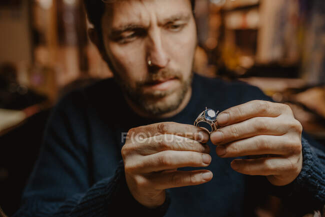Ювелир держит незаконченное кольцо в грязных руках и проверяет качество в мастерской — стоковое фото