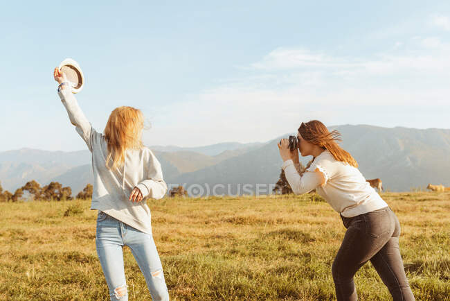 Vista laterale femminile scattare foto di bionda fidanzata alzando il braccio con cappello trascorrere del tempo insieme in montagna — Foto stock
