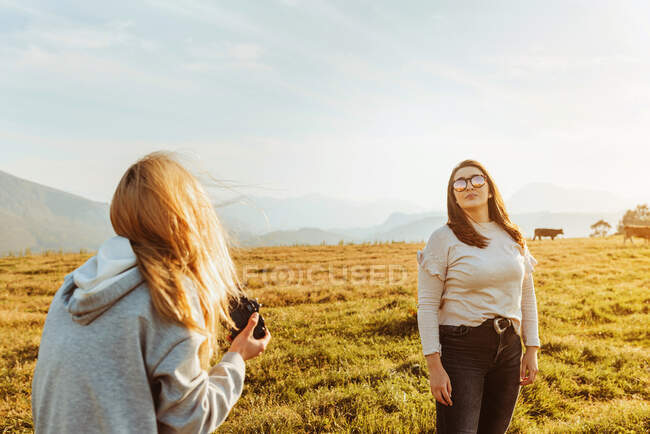 Vista posterior femenina tomar fotos de novia con gafas de sol y pasar tiempo juntos en las montañas - foto de stock